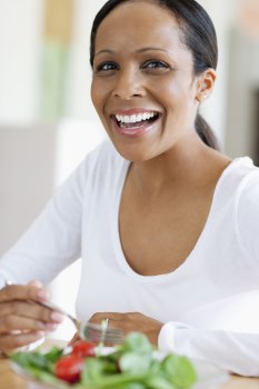 Making healthier food choices will help your body get the nutrients it needs without all the unnecessary calories. Photo of a woman looking at the camera and smiling. She is eating a green salad.