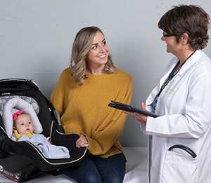 Woman with baby in carrier talking to doctor.